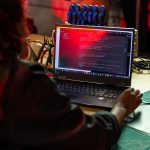Desenvolvedor de software escreve código em um laptop sobre uma bancada com ferramentas e componentes eletrônicos.