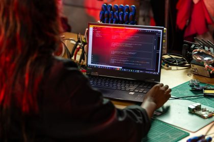 Desenvolvedor de software escreve código em um laptop sobre uma bancada com ferramentas e componentes eletrônicos.