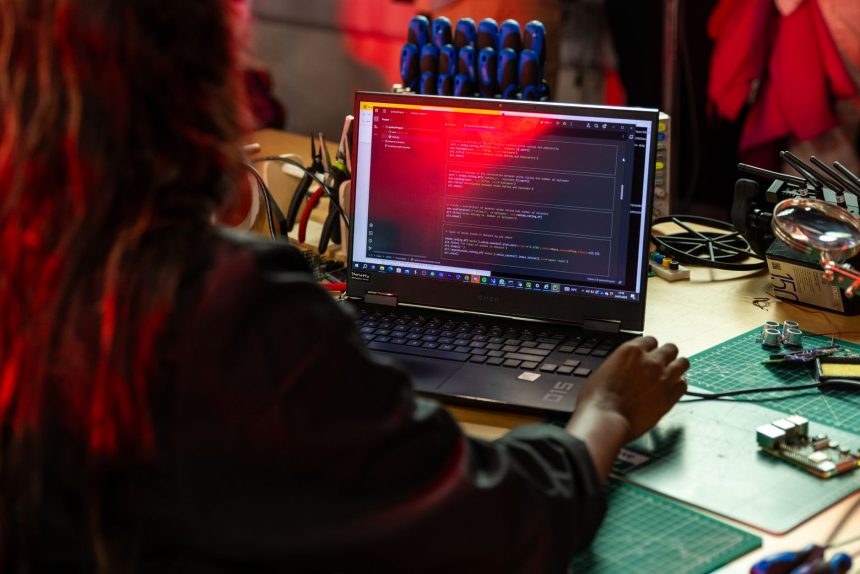 Desenvolvedor de software escreve código em um laptop sobre uma bancada com ferramentas e componentes eletrônicos.