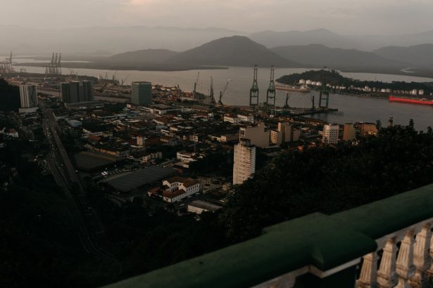 Vista aérea de uma área portuária com guindastes de carga, embarcações e casas às margens de um rio